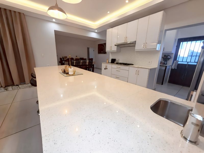 Modern open-plan kitchen featuring a large quartz island, sleek white cabinetry, integrated gas hob, and recessed ceiling lighting, flowing into the dining area.