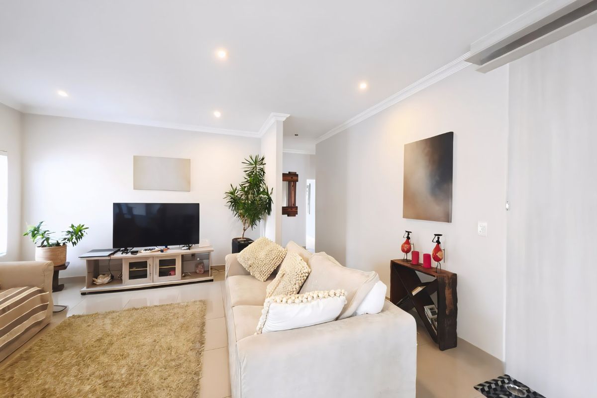 A bright and well-maintained living room featuring neutral tiled flooring, recessed downlighting, and crown molding, creating a clean and inviting atmosphere.