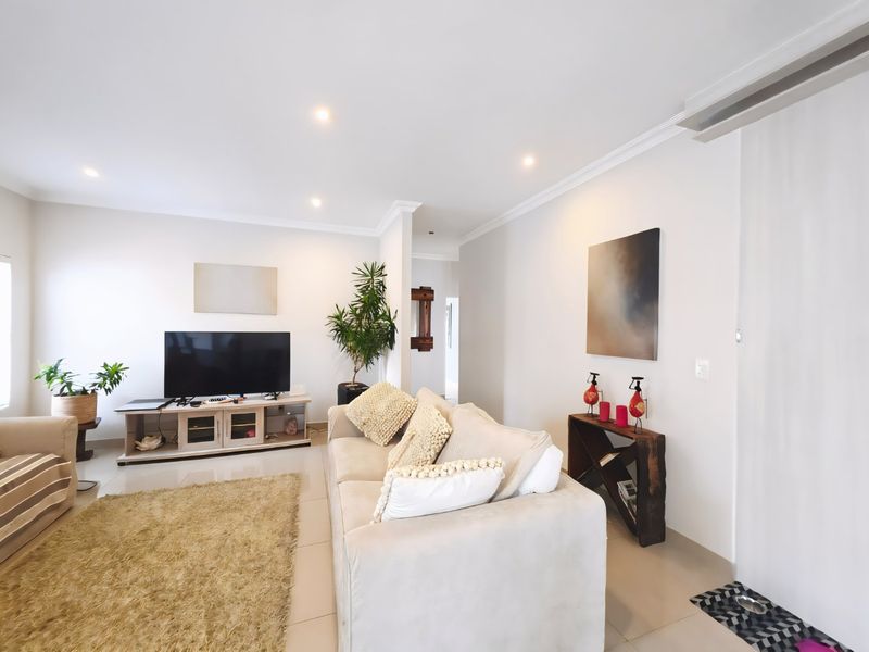 A bright and well-maintained living room featuring neutral tiled flooring, recessed downlighting, and crown molding, creating a clean and inviting atmosphere.