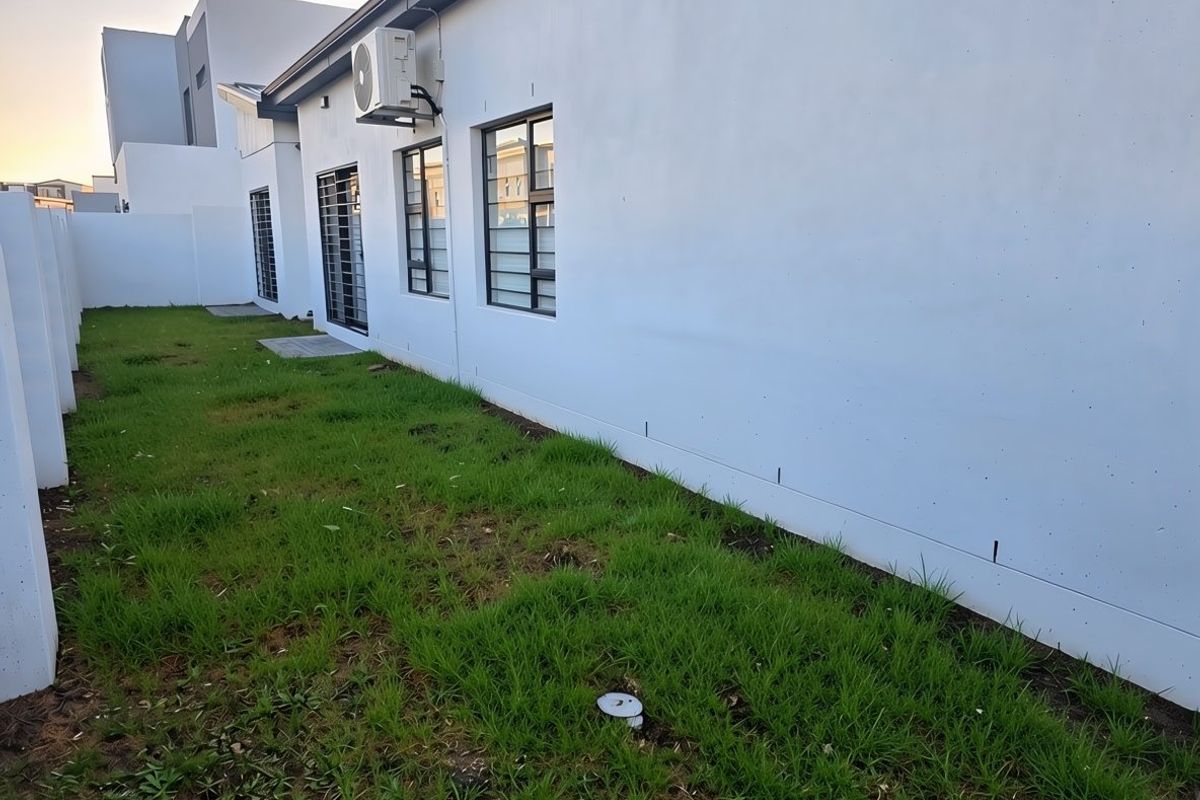 Rear exterior view of the property featuring a white rendered facade, security-fitted windows, and a private lawn area with an external air conditioning unit.