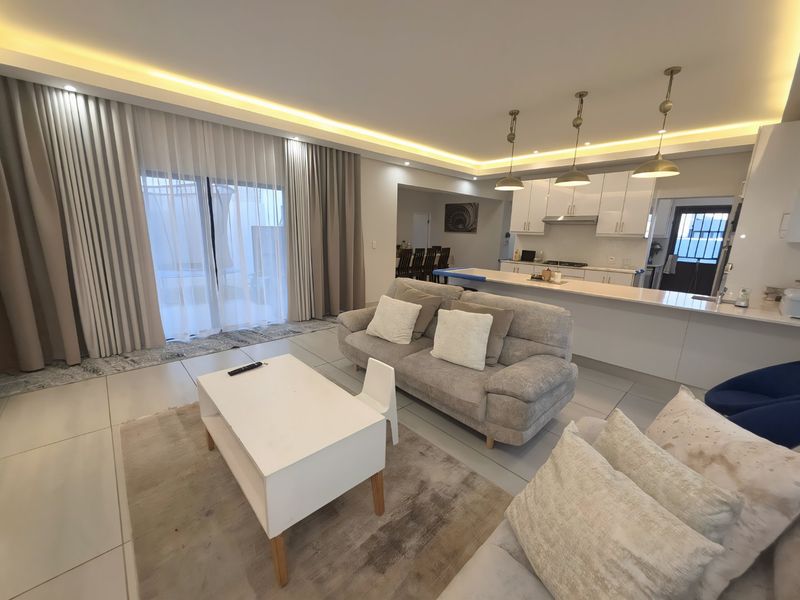 Modern open-plan living area featuring a sleek kitchen with island, recessed lighting, and large sliding doors leading to the outdoor space.