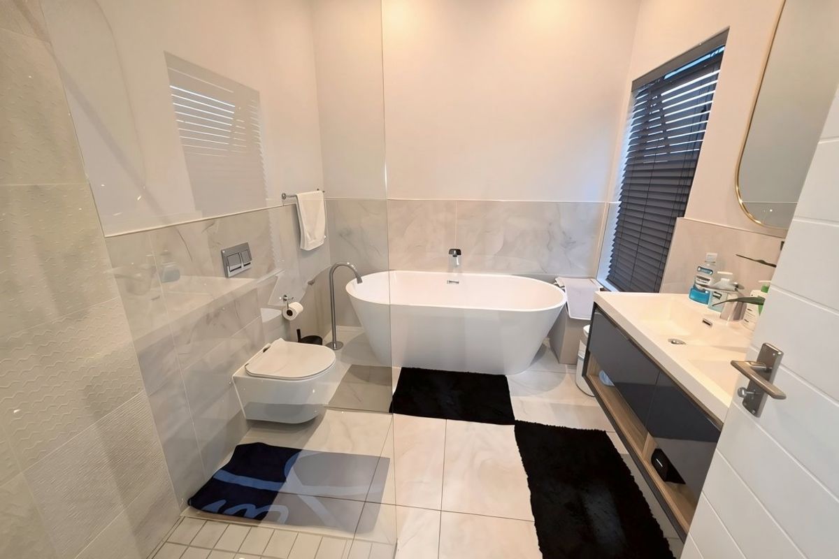 Modern bathroom featuring a sleek freestanding bathtub, wall-mounted toilet, and a contemporary vanity unit with integrated sink and high-quality tiled finishes.