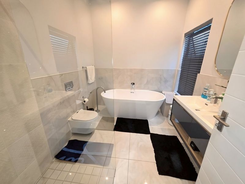 Modern bathroom featuring a sleek freestanding bathtub, wall-mounted toilet, and a contemporary vanity unit with integrated sink and high-quality tiled finishes.