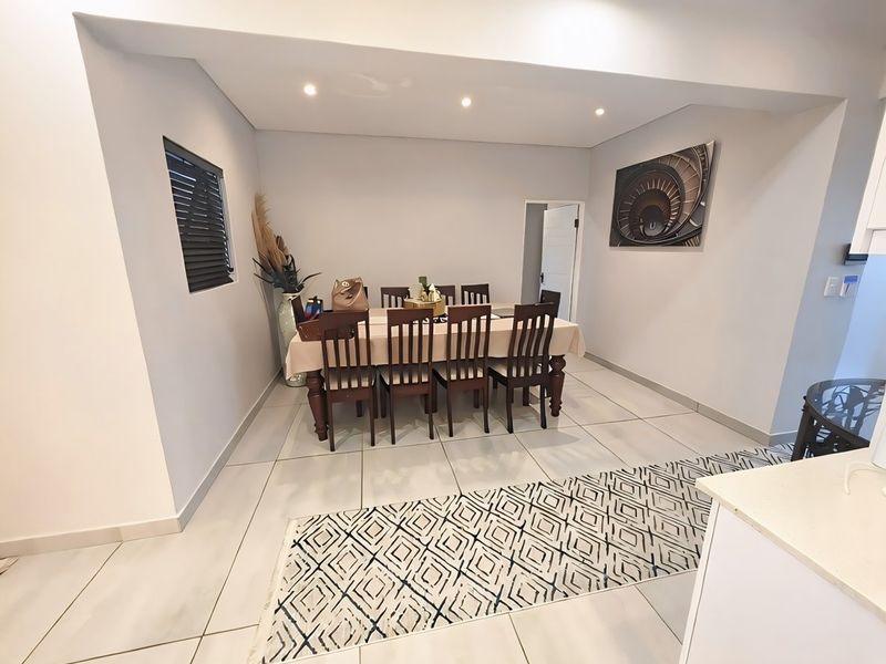 A bright and modern dining area featuring neutral wall tones, large format floor tiles, and recessed ceiling lighting.