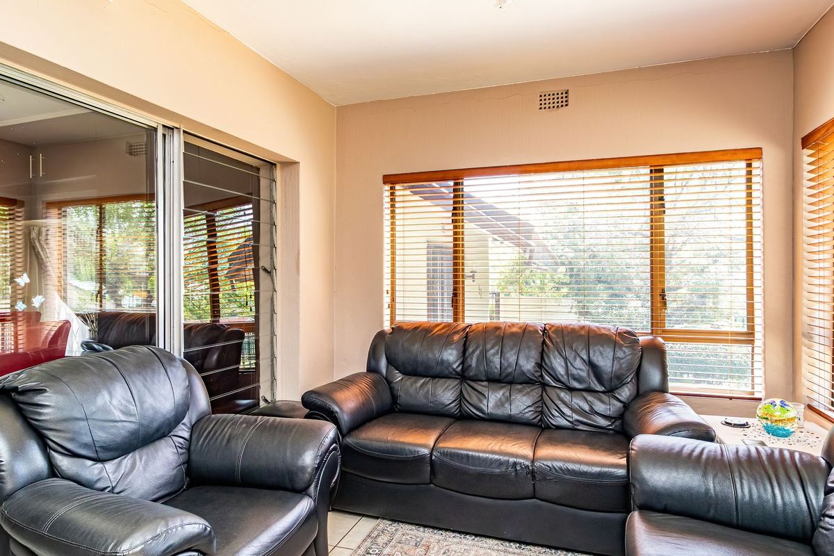 A bright living room featuring large windows with venetian blinds, tiled flooring, and sliding glass doors leading to an outdoor area.