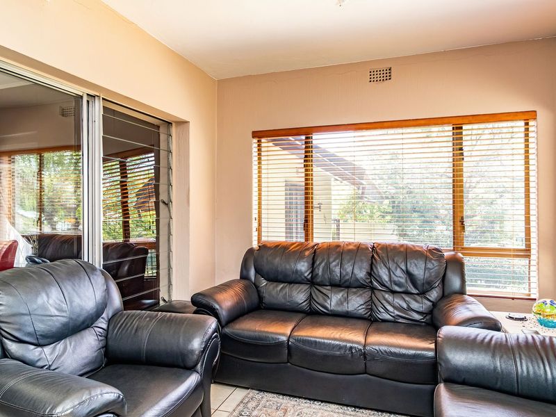 A bright living room featuring large windows with venetian blinds, tiled flooring, and sliding glass doors leading to an outdoor area.