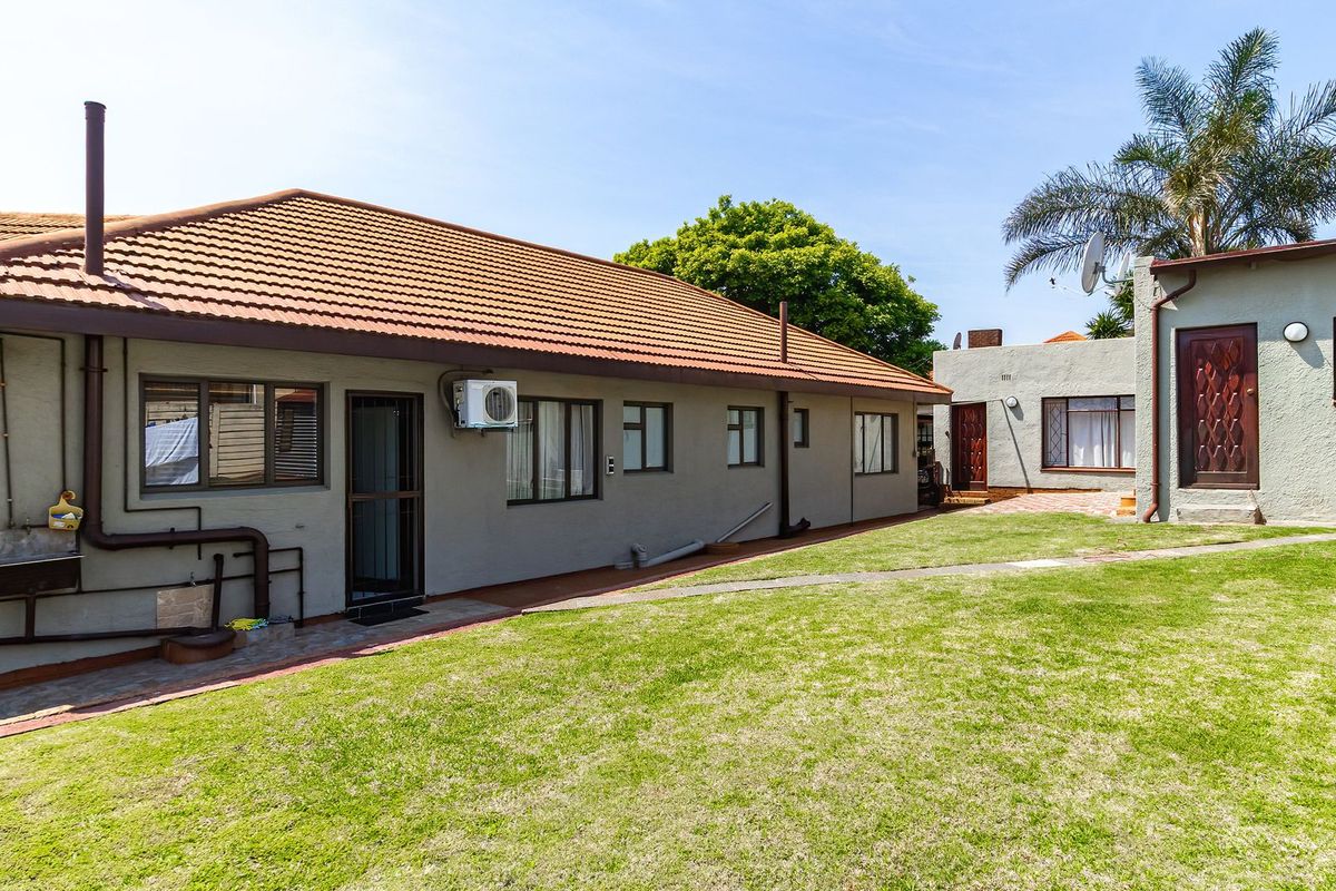 Rear view of the house featuring a tiled roof, paved walkway, and a well-maintained lawn area.