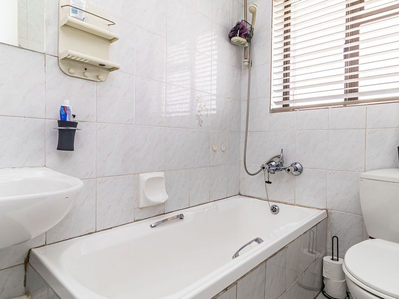 A functional bathroom featuring a bathtub with shower mixer, pedestal basin, and toilet, finished with tiled walls and fitted window blinds.