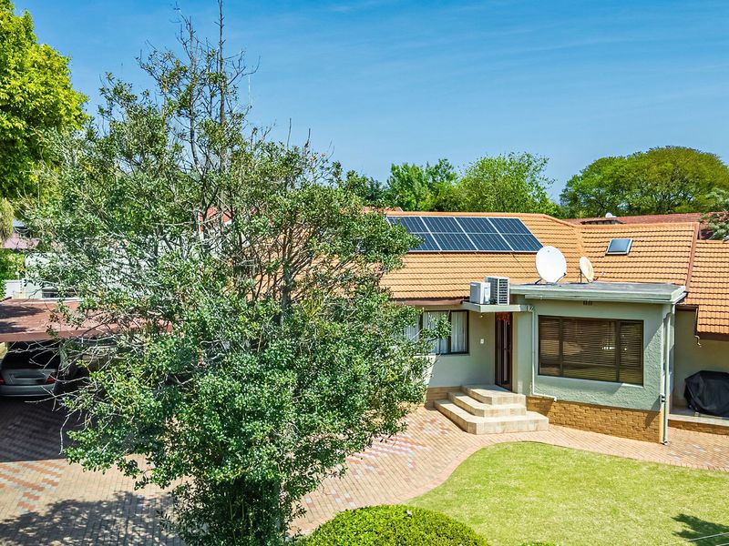 Rear view of a residential property featuring a tiled roof with solar panels, a paved driveway, a carport, and a landscaped garden area.