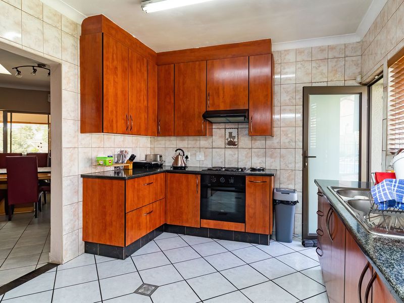 A functional kitchen featuring warm-toned wooden cabinetry, granite countertops, built-in oven, gas hob, and tiled finishes throughout.