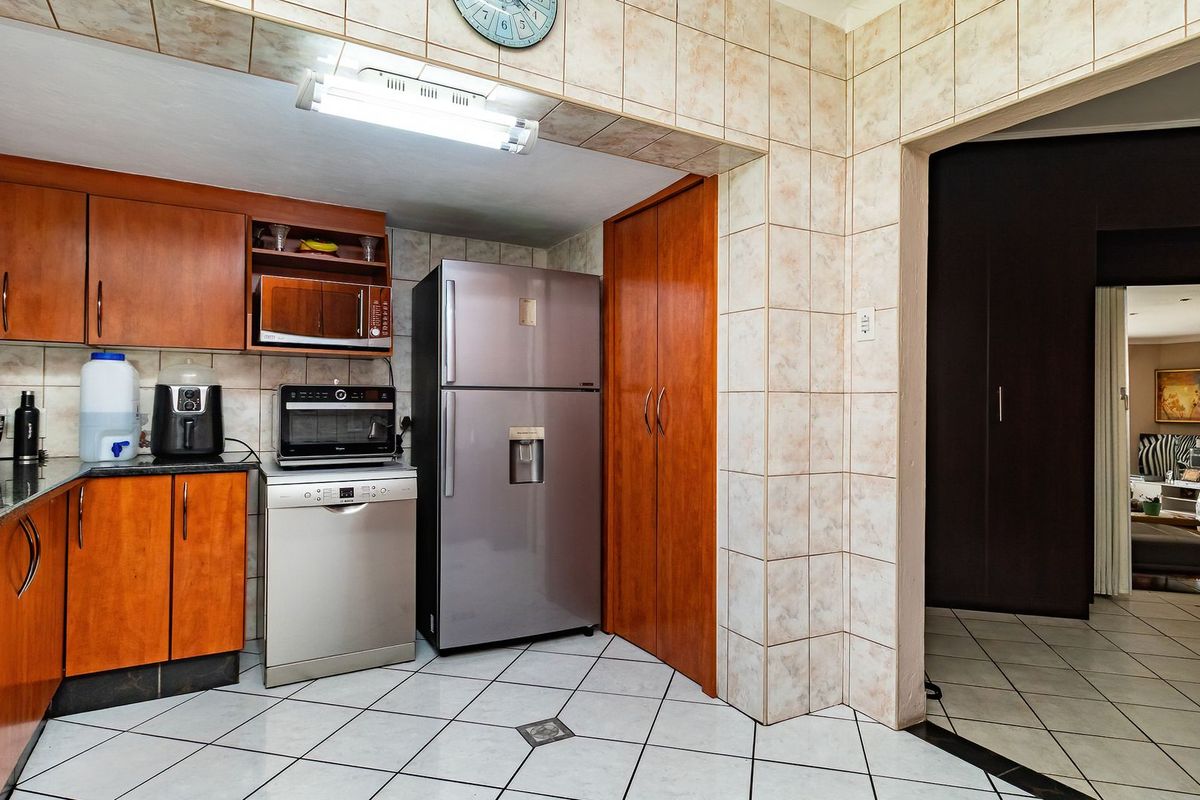 A functional kitchen featuring wood-finish cabinetry, granite countertops, tiled backsplash, and tiled flooring, with a built-in pantry and direct access to the living area.