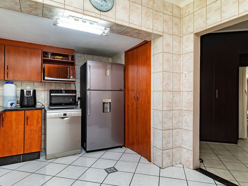A functional kitchen featuring wood-finish cabinetry, granite countertops, tiled backsplash, and tiled flooring, with a built-in pantry and direct access to the living area.
