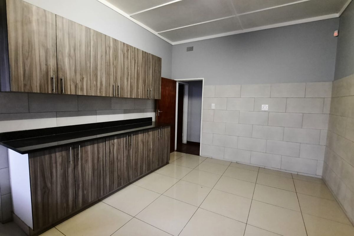 A clean, empty kitchen featuring modern wood-grain cabinetry, dark stone countertops, and neutral tiled walls and flooring.