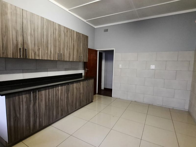 A clean, empty kitchen featuring modern wood-grain cabinetry, dark stone countertops, and neutral tiled walls and flooring.
