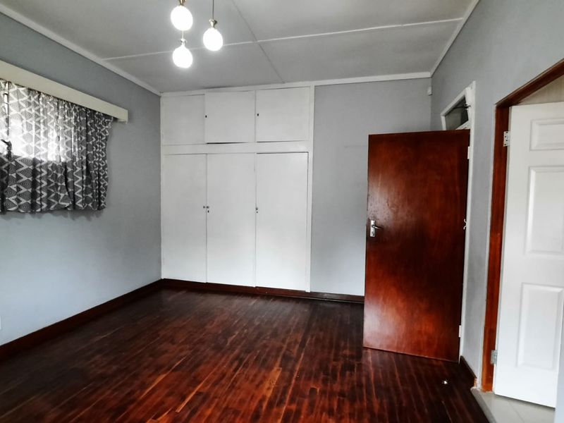 A spacious bedroom featuring polished hardwood flooring, built-in storage cupboards, and neutral wall tones, offering a clean and versatile living space.