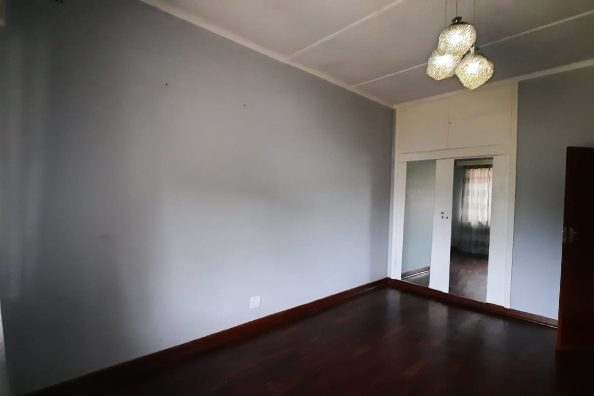 An empty bedroom featuring polished hardwood flooring, built-in cupboards with mirrored doors, and a central ceiling light fixture.