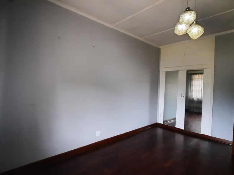 An empty bedroom featuring polished hardwood flooring, built-in cupboards with mirrored doors, and a central ceiling light fixture.