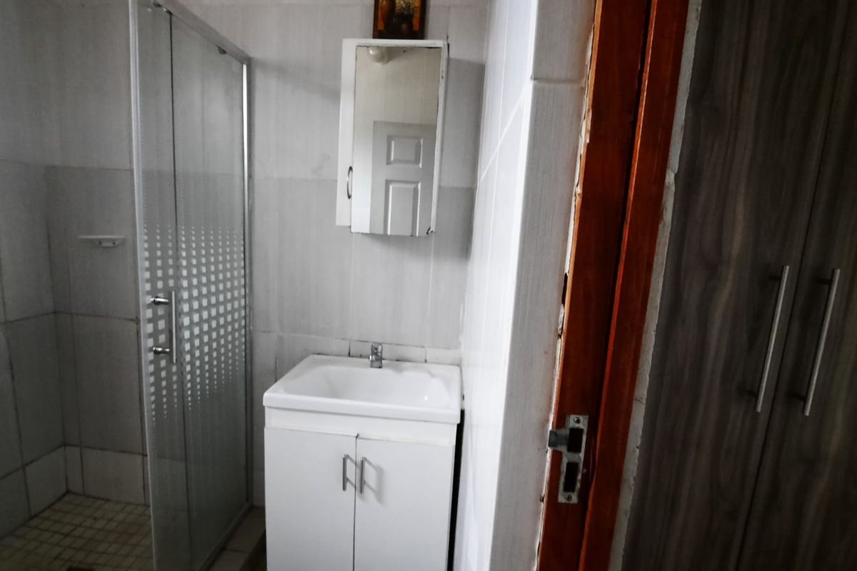 A functional bathroom featuring a shower enclosure, vanity basin with storage, and a wall-mounted medicine cabinet, finished with tiled walls.