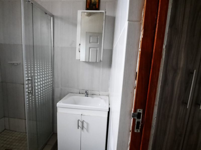 A functional bathroom featuring a shower enclosure, vanity basin with storage, and a wall-mounted medicine cabinet, finished with tiled walls.
