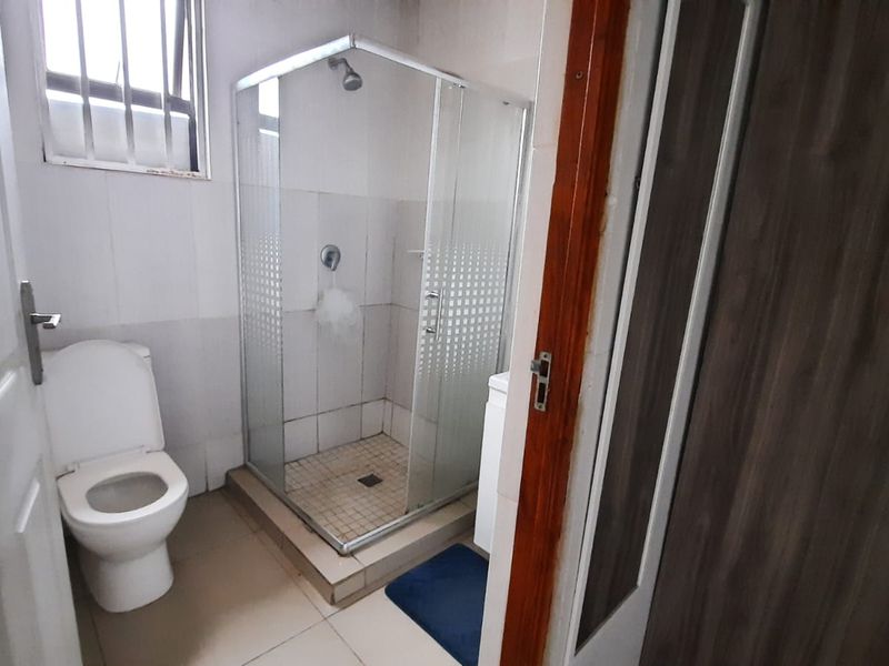 A functional bathroom featuring a glass-enclosed shower, standard toilet, and tiled finishes throughout, offering a clean and practical layout.