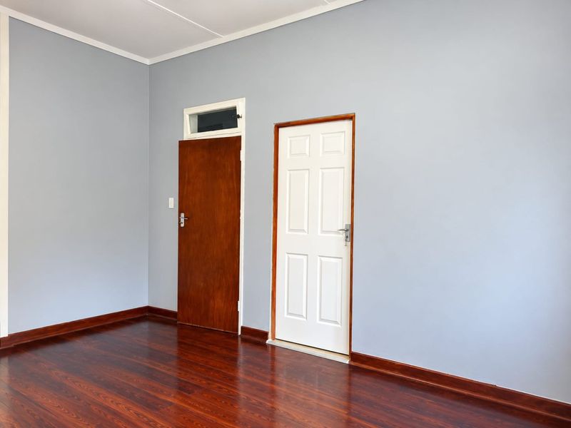 A clean, empty bedroom featuring polished hardwood flooring, neutral grey walls, and two distinct interior doors with a transom window above one.
