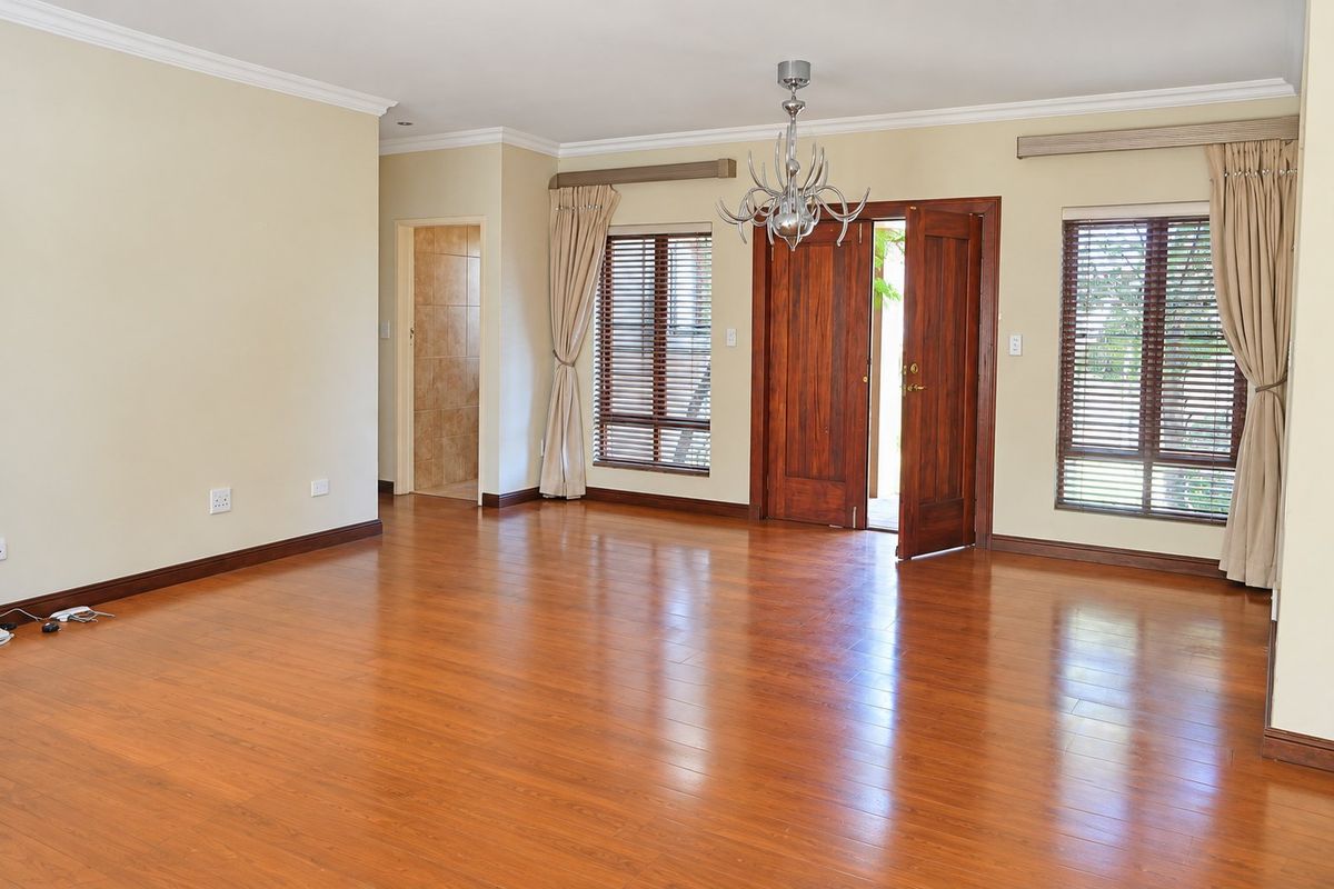 Spacious living area featuring warm laminate flooring, timber door access to the exterior, and large windows with fitted blinds.