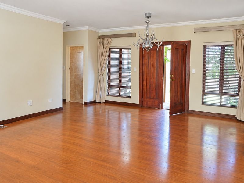 Spacious living area featuring warm laminate flooring, timber door access to the exterior, and large windows with fitted blinds.