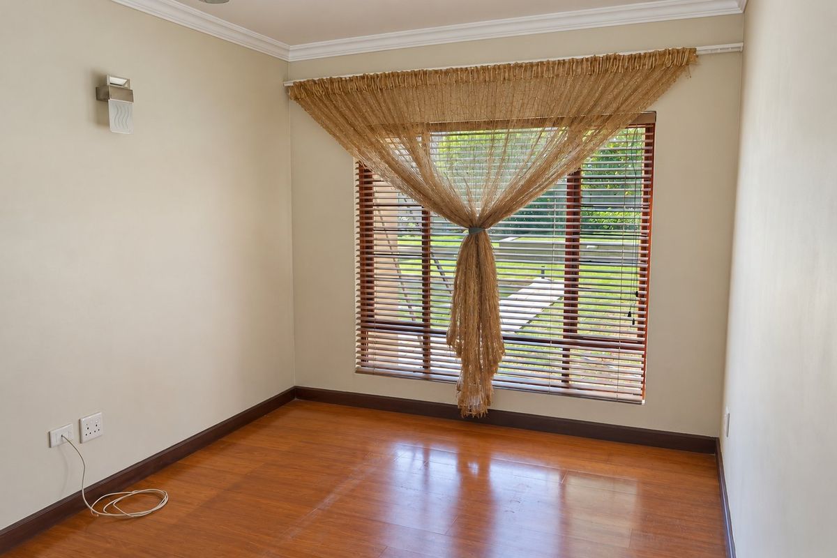 A bright, empty bedroom featuring warm-toned laminate flooring, timber venetian blinds, and neutral wall finishes, offering a clean canvas for personalization.