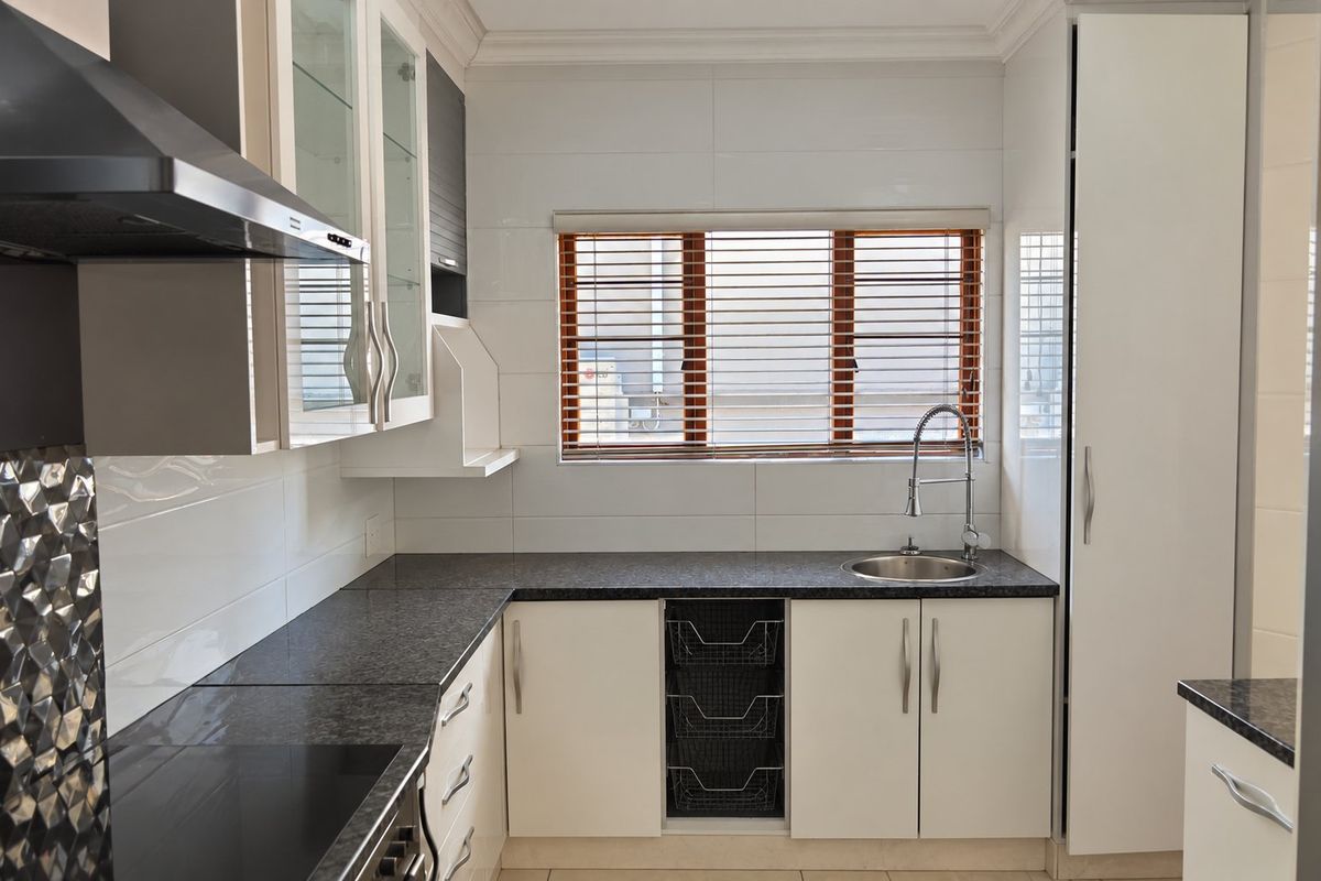 A clean, modern kitchen featuring granite countertops, white cabinetry, a stainless steel sink, and a built-in extractor fan.