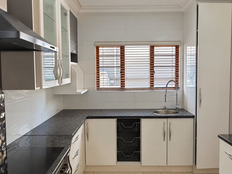 A clean, modern kitchen featuring granite countertops, white cabinetry, a stainless steel sink, and a built-in extractor fan.
