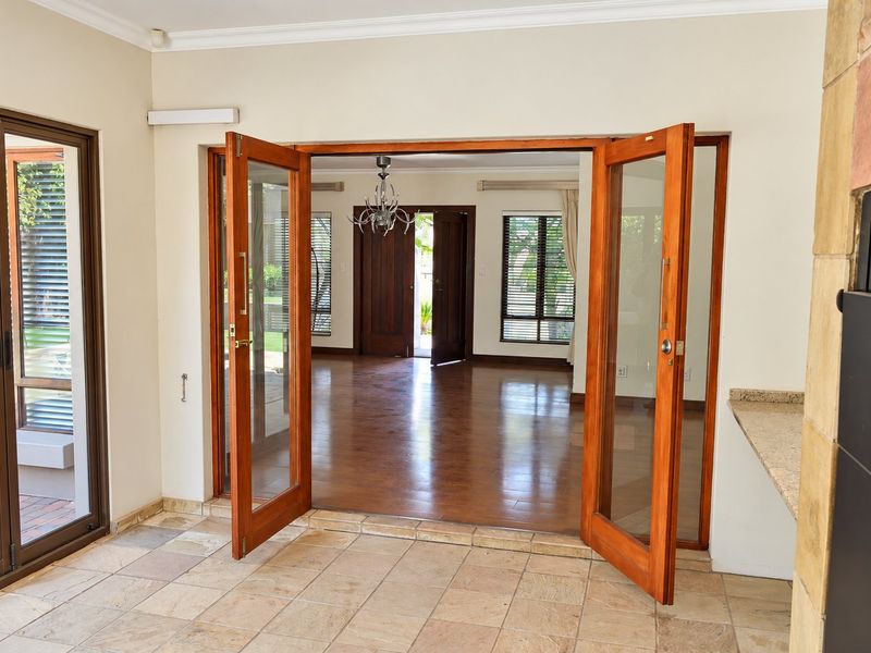 Spacious living area featuring stone tile flooring, wooden double doors leading to an adjacent room with laminate flooring, and a built-in fireplace.