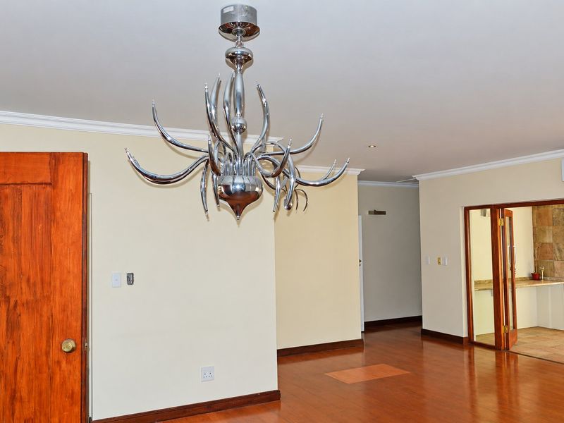 Spacious living area featuring laminated timber flooring, crown molding, and recessed lighting, with direct access to an adjacent room through glass-paneled double doors.