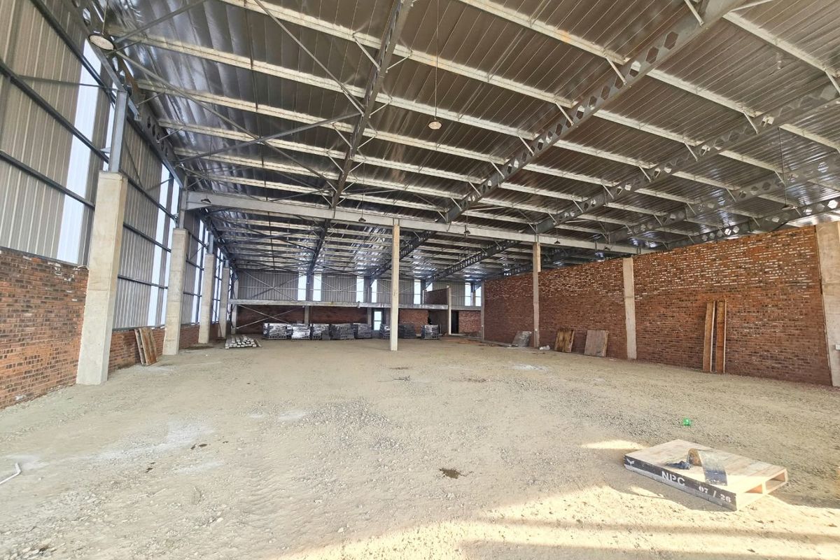 Large industrial warehouse space featuring exposed steel roof trusses, brick walls, and concrete columns, currently in an unfinished shell condition.