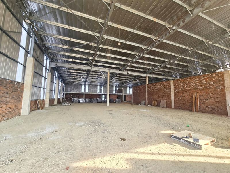 Large industrial warehouse space featuring exposed steel roof trusses, brick walls, and concrete columns, currently in an unfinished shell condition.