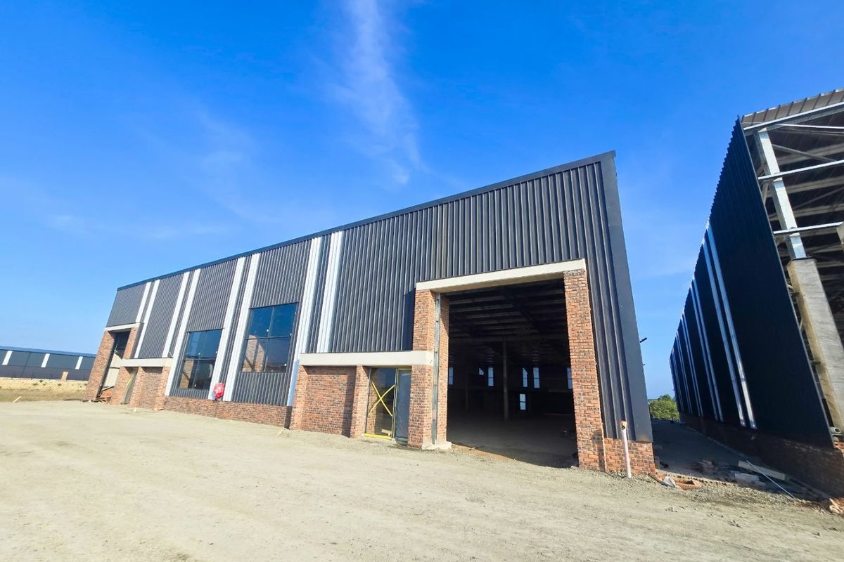 Modern industrial warehouse building featuring corrugated metal cladding, exposed brick accents, and large open bays under a clear blue sky.