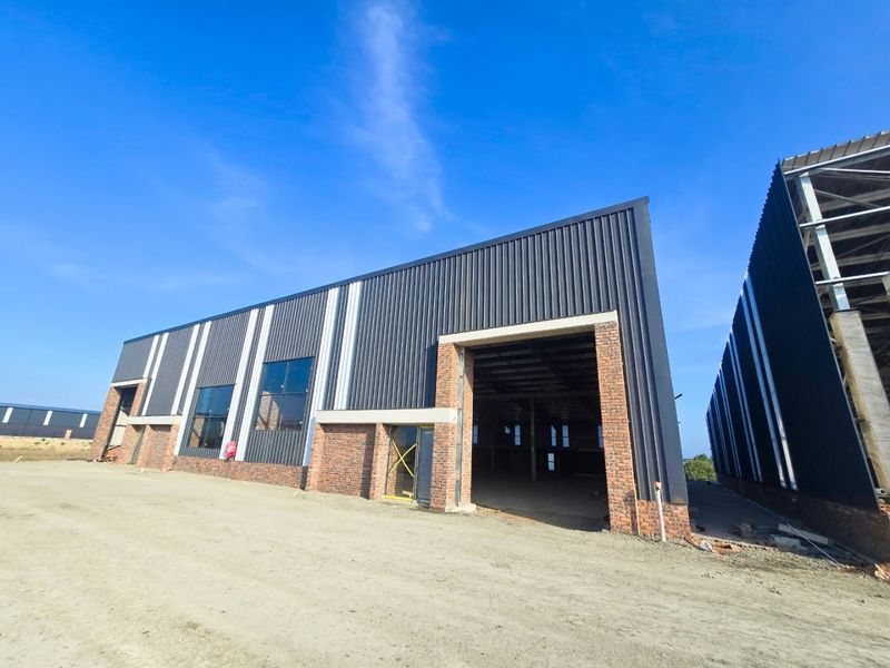 Modern industrial warehouse building featuring corrugated metal cladding, exposed brick accents, and large open bays under a clear blue sky.