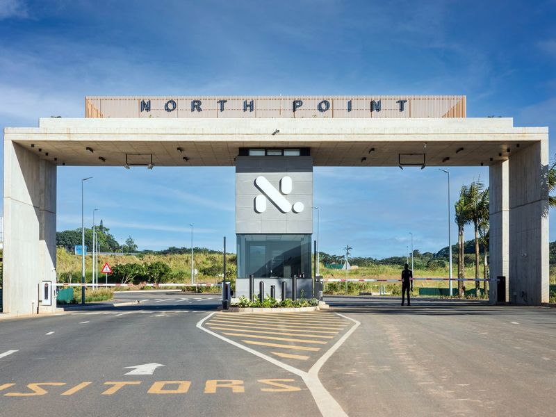 Modern industrial park entrance featuring a concrete portal frame, security gatehouse, and automated boom gates.
