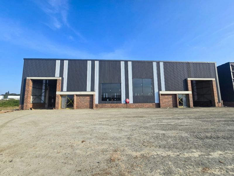 Modern industrial warehouse facade featuring corrugated metal cladding, face brick accents, and large windows, currently in the final stages of construction.