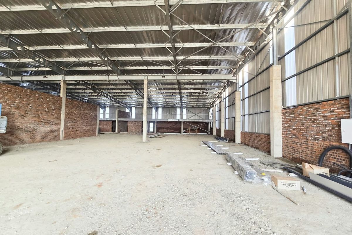 A large, open-plan industrial warehouse space featuring exposed brick walls, steel roof trusses, and concrete flooring, suitable for various commercial or industrial applications.