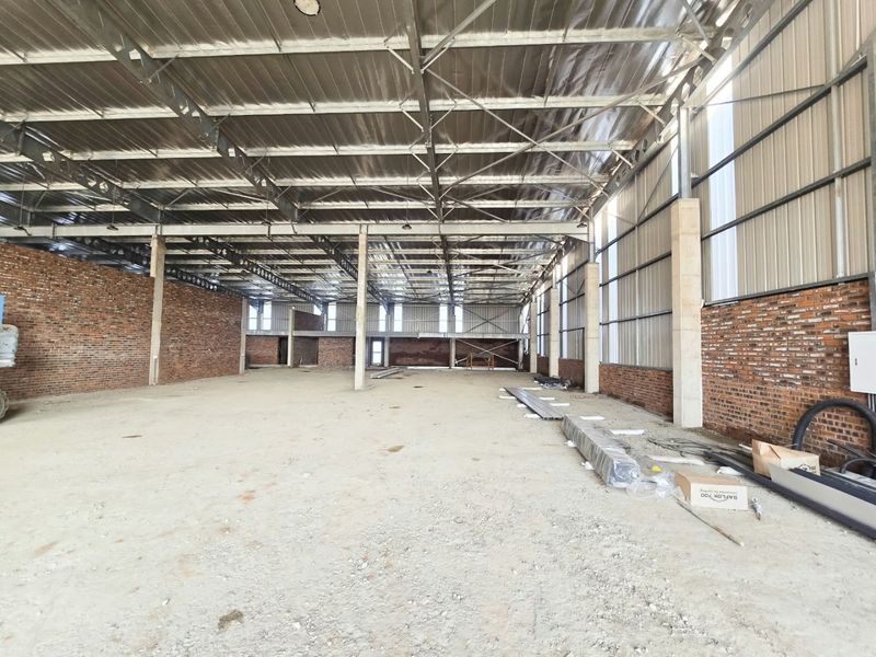 A large, open-plan industrial warehouse space featuring exposed brick walls, steel roof trusses, and concrete flooring, suitable for various commercial or industrial applications.