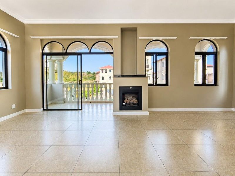 Spacious living area featuring tiled floors, a built-in fireplace, and large arched windows with direct access to a balcony.