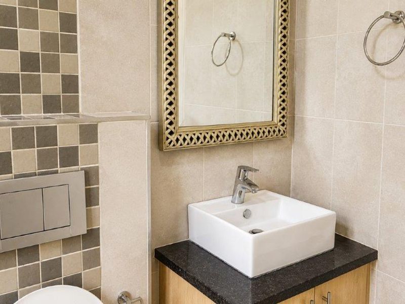 A modern bathroom featuring a vessel sink on a granite countertop, vanity cabinet, and wall-mounted toilet flush plate with decorative tiled accents.