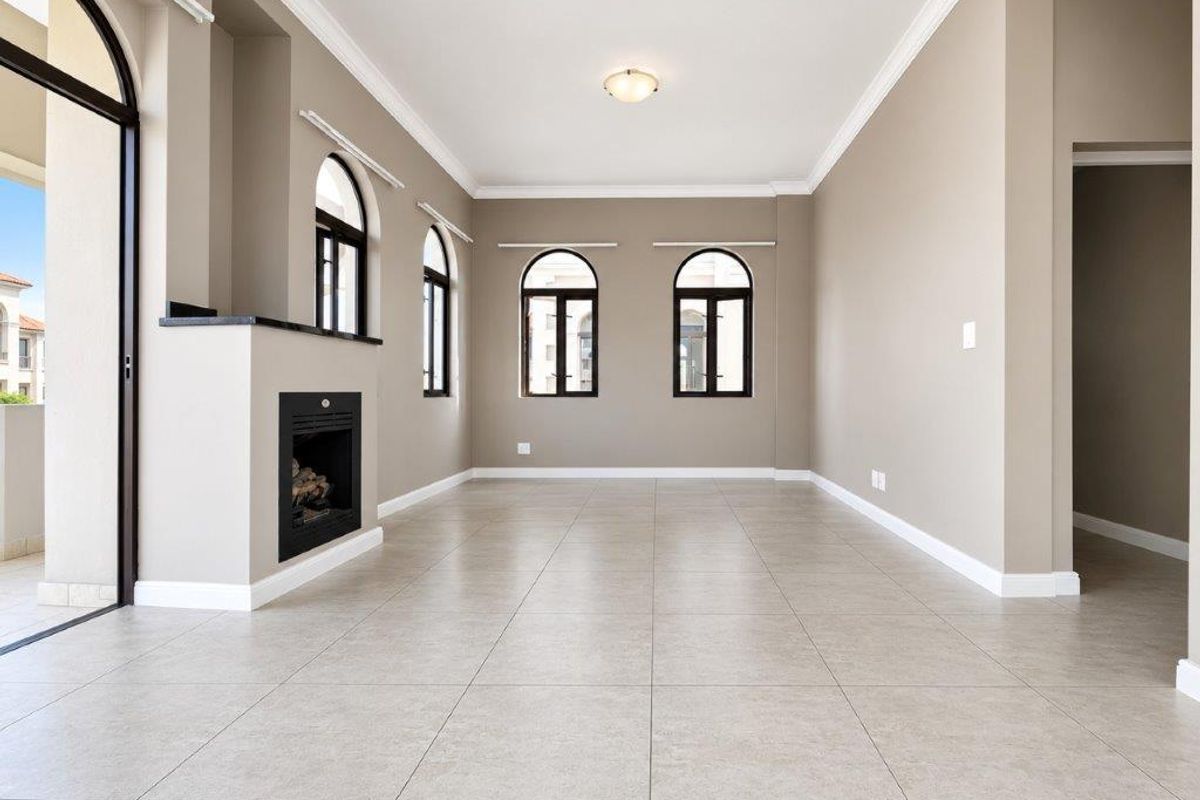 Spacious, light-filled living room featuring neutral tiled floors, a built-in fireplace, and elegant arched windows with access to an outdoor patio area.