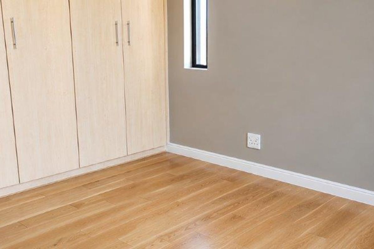 A clean, empty bedroom featuring light timber flooring, neutral wall tones, and modern built-in cupboards with sleek hardware.