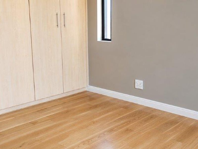 A clean, empty bedroom featuring light timber flooring, neutral wall tones, and modern built-in cupboards with sleek hardware.
