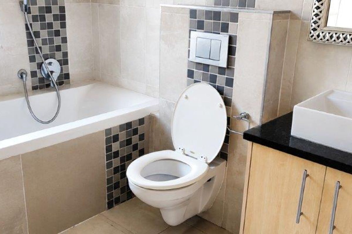 Modern bathroom featuring a built-in bathtub, wall-mounted toilet, and a vanity cabinet with a countertop basin and tiled accents.
