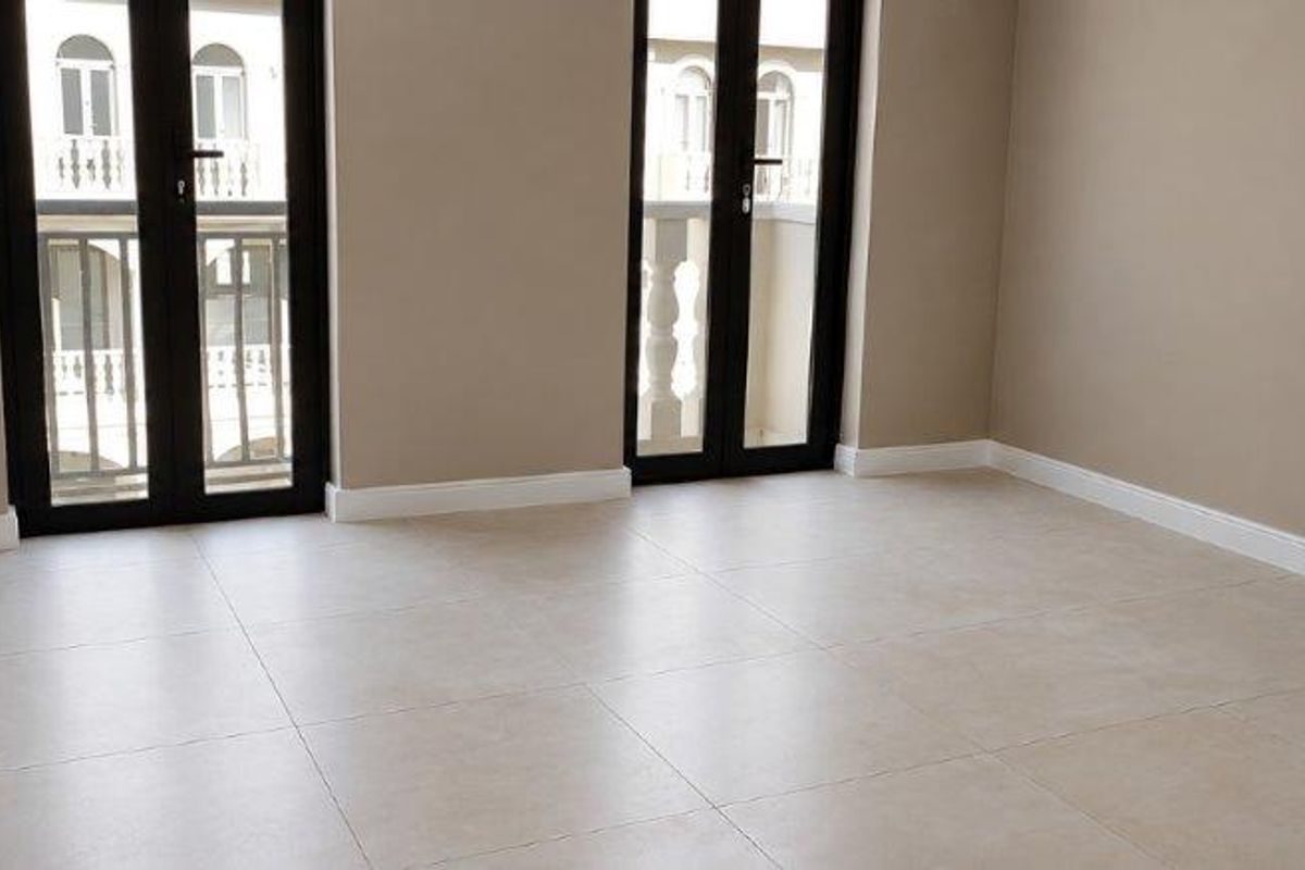 A bright, empty bedroom featuring neutral tiled flooring, built-in cupboards, and two sets of double french doors leading to a balcony.