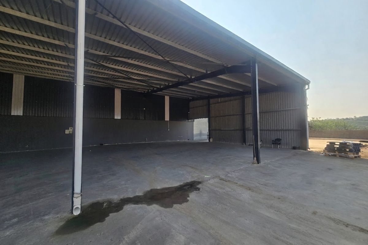Spacious industrial warehouse area featuring high-clearance corrugated metal roofing, steel support columns, and durable concrete flooring, suitable for storage or manufacturing operations.