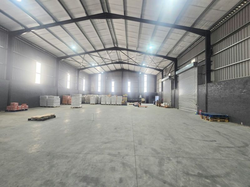 Spacious industrial warehouse featuring high ceilings, concrete flooring, steel portal frame construction, and a large roller shutter door for efficient access.