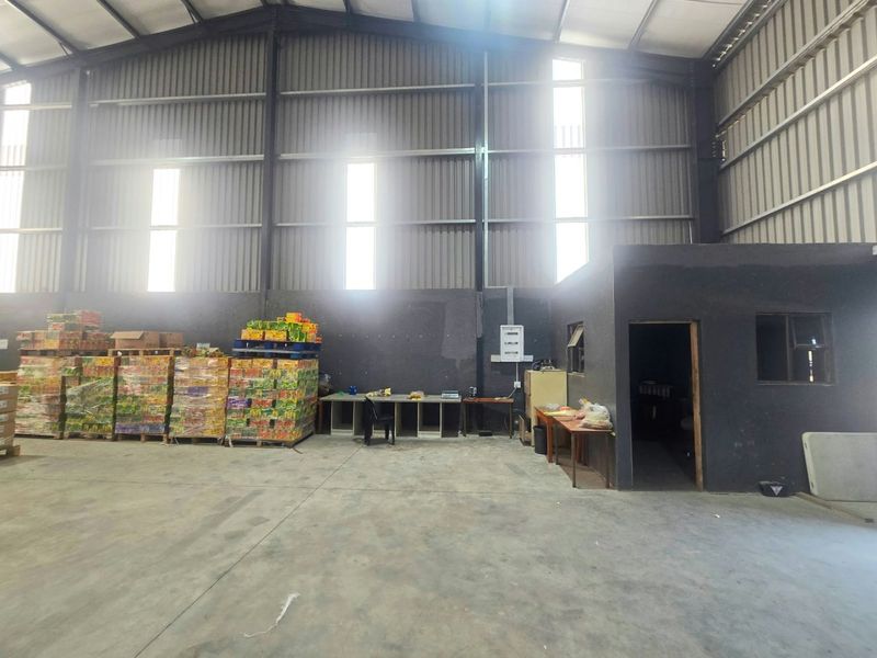 Spacious industrial warehouse featuring high-clearance steel portal frame construction, corrugated metal walls, concrete flooring, and integrated office or storage enclosure.